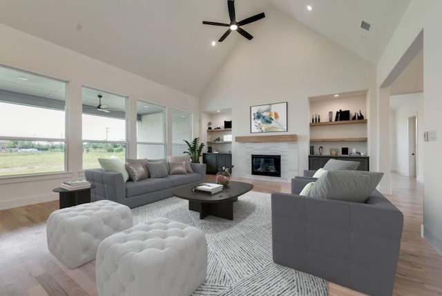 living room featuring a tiled fireplace, light hardwood / wood-style flooring, built in features, and ceiling fan