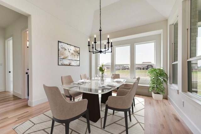 dining space with a notable chandelier, vaulted ceiling, and light hardwood / wood-style floors