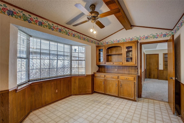 kitchen featuring lofted ceiling with beams, ceiling fan, a textured ceiling, and wooden walls