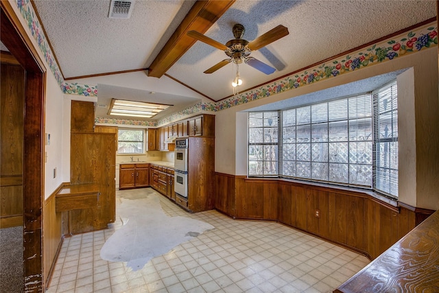 kitchen featuring wooden walls, sink, vaulted ceiling with beams, stainless steel double oven, and a textured ceiling