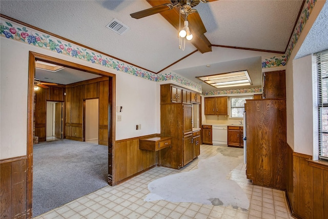 kitchen featuring white dishwasher, vaulted ceiling with beams, wooden walls, and a textured ceiling