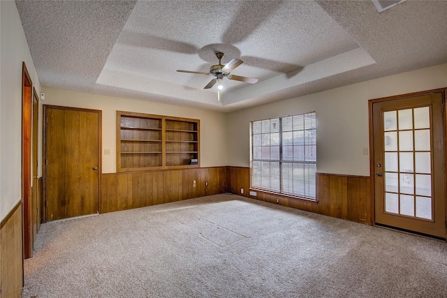 unfurnished room with a textured ceiling, wooden walls, and a tray ceiling