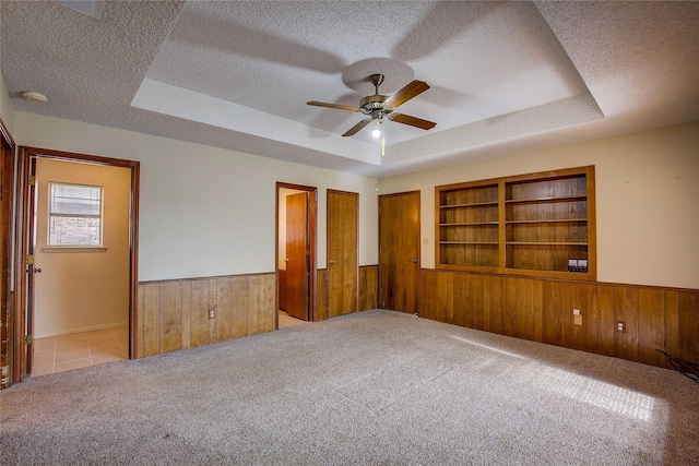 carpeted empty room featuring a raised ceiling, a textured ceiling, wooden walls, and built in shelves