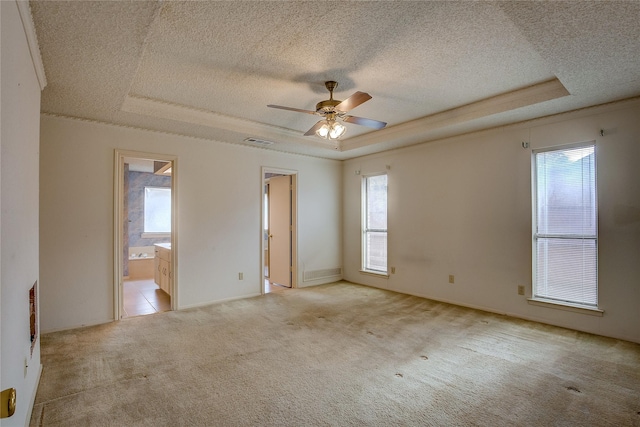 unfurnished room with ceiling fan, light colored carpet, a tray ceiling, and a textured ceiling