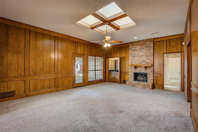 unfurnished living room with wooden walls, a skylight, light colored carpet, a brick fireplace, and a textured ceiling