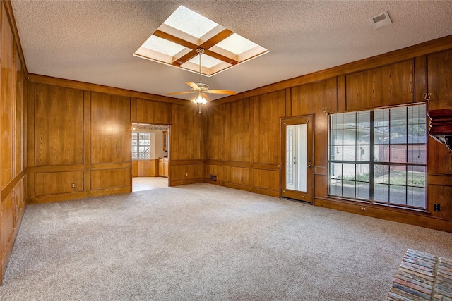 carpeted spare room featuring ceiling fan, a skylight, a textured ceiling, and wood walls