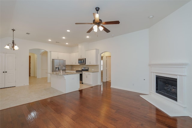 kitchen featuring hanging light fixtures, appliances with stainless steel finishes, a kitchen island with sink, light hardwood / wood-style floors, and white cabinets