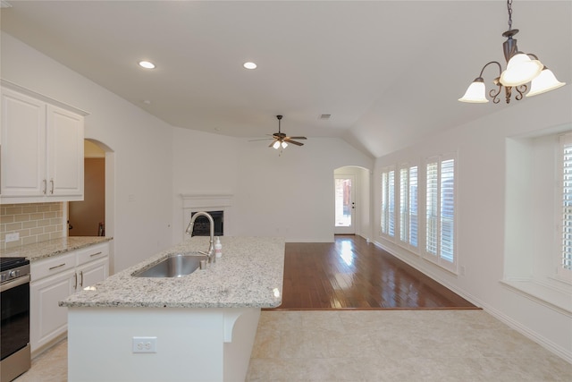 kitchen with sink, decorative light fixtures, a center island with sink, stainless steel stove, and white cabinets