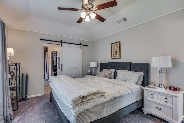 bedroom featuring dark colored carpet, a walk in closet, a raised ceiling, ceiling fan, and a barn door