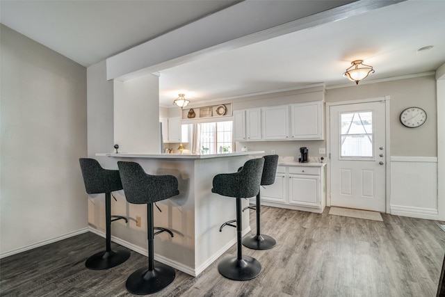 kitchen with a breakfast bar, white cabinets, kitchen peninsula, a healthy amount of sunlight, and light hardwood / wood-style flooring