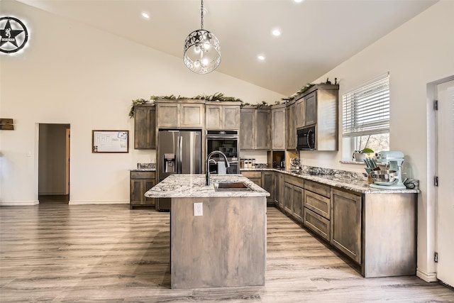 kitchen with light stone counters, a kitchen island with sink, a sink, and black appliances