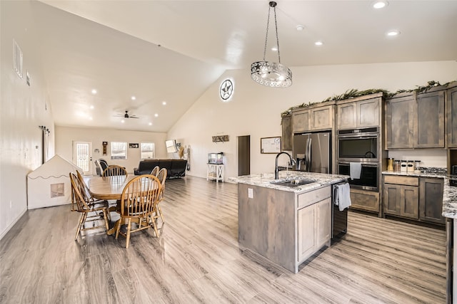 kitchen with an island with sink, appliances with stainless steel finishes, open floor plan, decorative light fixtures, and a sink