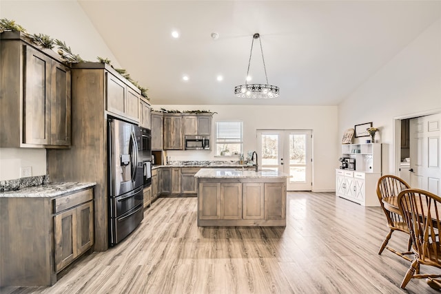 kitchen featuring appliances with stainless steel finishes, a kitchen island with sink, hanging light fixtures, and light stone countertops