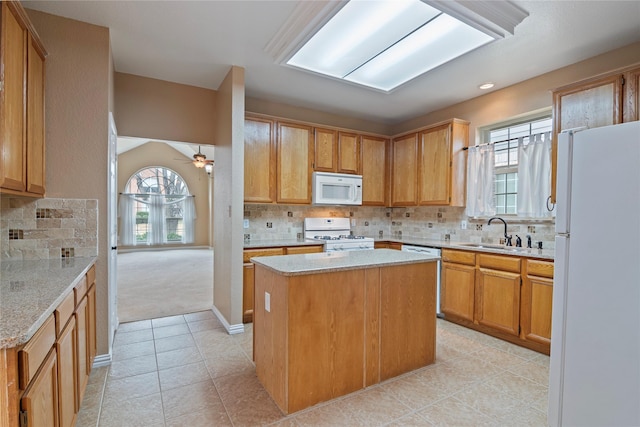 kitchen featuring sink, white appliances, backsplash, light stone counters, and a kitchen island