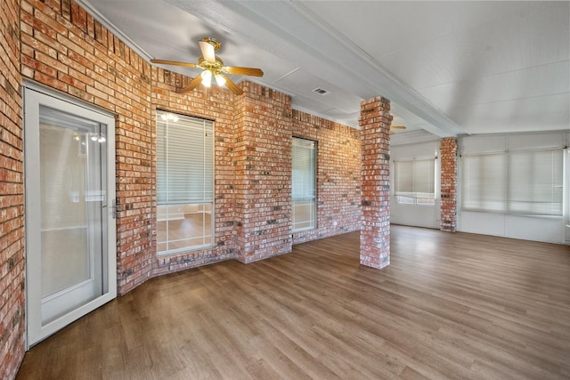 unfurnished living room with beam ceiling, hardwood / wood-style flooring, decorative columns, and brick wall