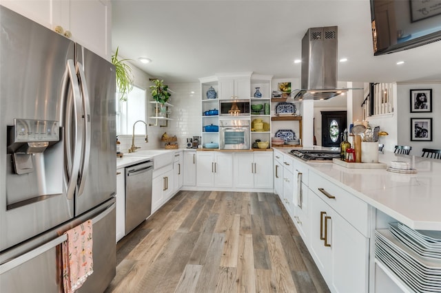 kitchen with sink, appliances with stainless steel finishes, island range hood, white cabinets, and light wood-type flooring