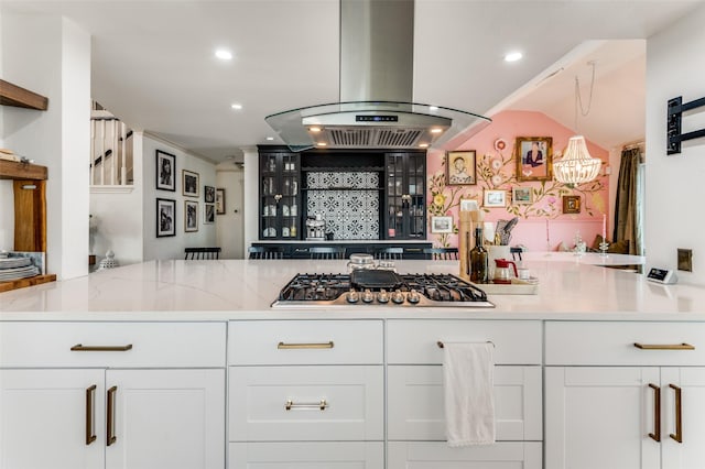 kitchen with stainless steel gas stovetop, island exhaust hood, light stone countertops, and white cabinetry