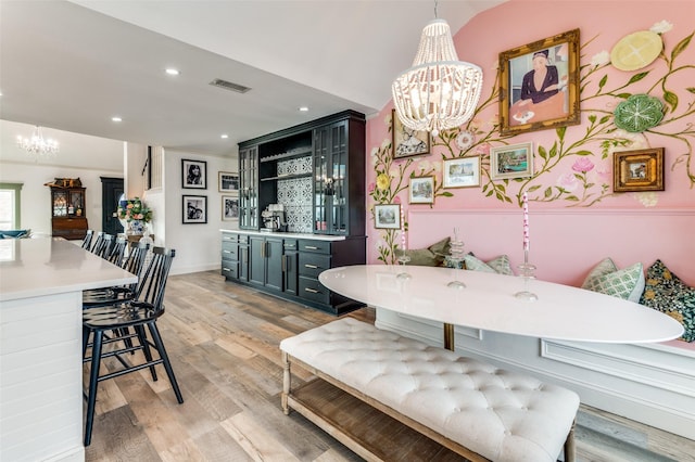 dining area featuring bar area, a notable chandelier, lofted ceiling, and light wood-type flooring