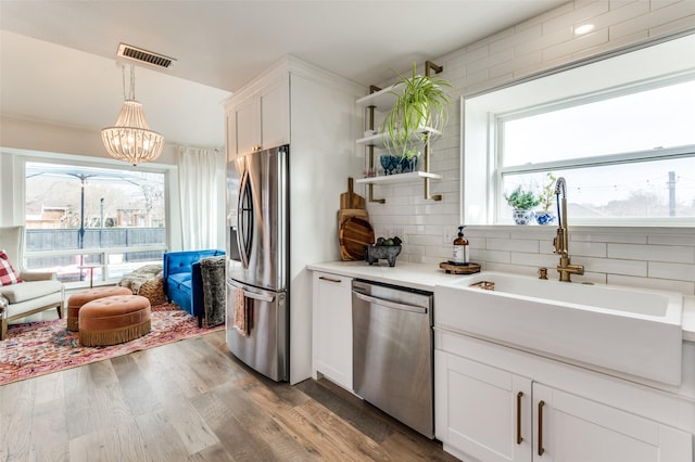 kitchen with sink, dark wood-type flooring, stainless steel appliances, white cabinets, and decorative light fixtures