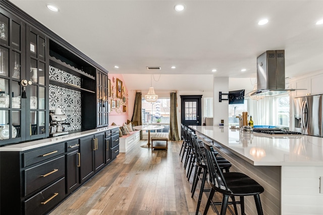 kitchen with appliances with stainless steel finishes, a breakfast bar area, hanging light fixtures, island exhaust hood, and a spacious island