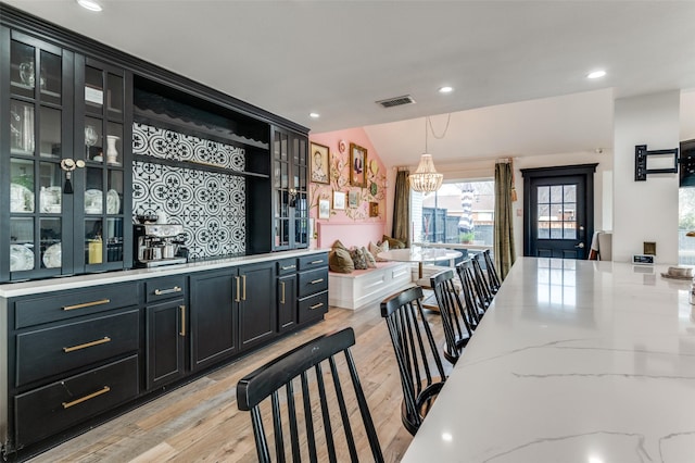 kitchen with a breakfast bar, light stone counters, vaulted ceiling, light wood-type flooring, and pendant lighting