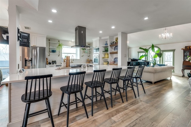 kitchen featuring appliances with stainless steel finishes, white cabinets, a kitchen bar, island exhaust hood, and kitchen peninsula