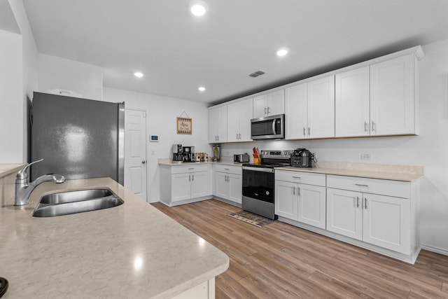 kitchen with appliances with stainless steel finishes, sink, white cabinets, and light hardwood / wood-style flooring