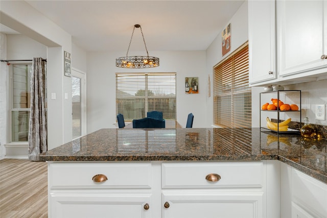 kitchen featuring decorative light fixtures, dark stone countertops, white cabinets, light hardwood / wood-style floors, and backsplash