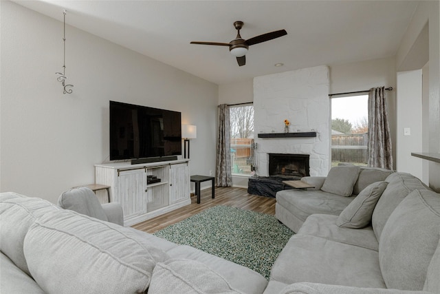 living room featuring ceiling fan, a stone fireplace, and light wood-type flooring