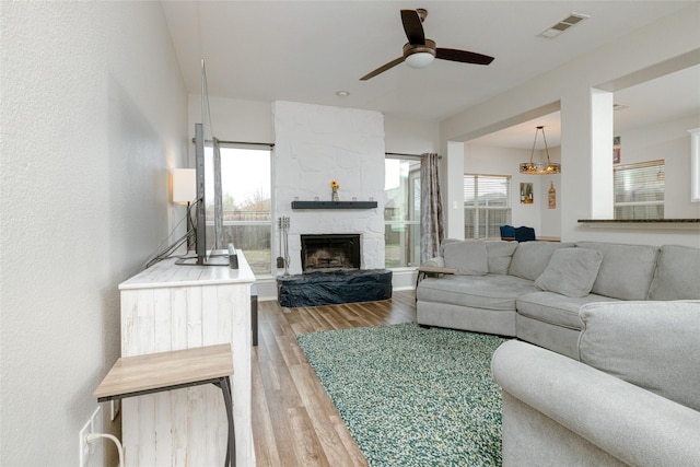 living room featuring a wealth of natural light, a stone fireplace, hardwood / wood-style floors, and ceiling fan