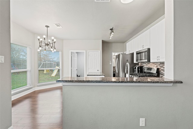 kitchen featuring pendant lighting, stainless steel appliances, kitchen peninsula, and white cabinets