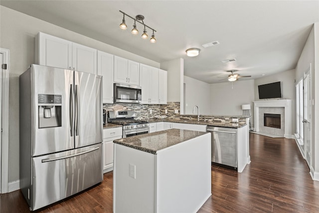 kitchen featuring appliances with stainless steel finishes, dark stone countertops, a center island, white cabinets, and kitchen peninsula