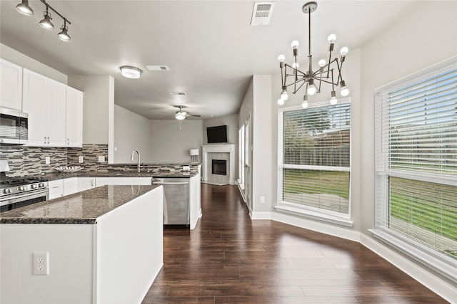 kitchen featuring ceiling fan with notable chandelier, appliances with stainless steel finishes, dark stone countertops, decorative backsplash, and decorative light fixtures