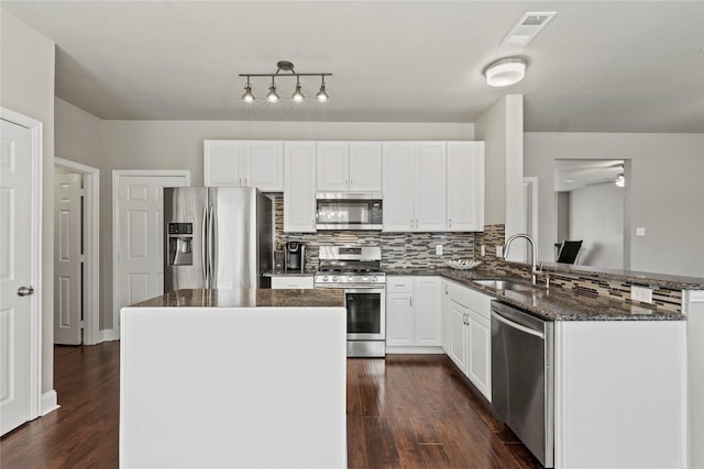 kitchen featuring sink, appliances with stainless steel finishes, dark stone countertops, white cabinetry, and kitchen peninsula