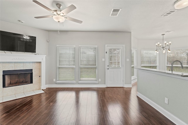 unfurnished living room featuring sink, dark hardwood / wood-style floors, ceiling fan with notable chandelier, and a fireplace