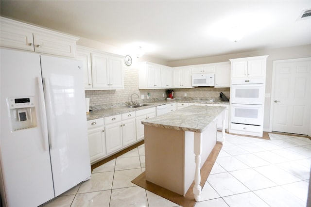 kitchen featuring sink, white appliances, light tile patterned floors, white cabinetry, and a kitchen island