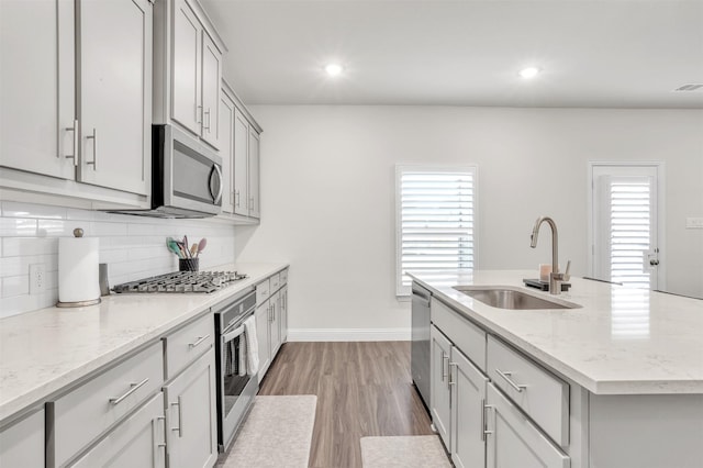 kitchen featuring tasteful backsplash, an island with sink, sink, light stone counters, and stainless steel appliances