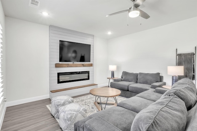 living room featuring hardwood / wood-style flooring, a large fireplace, and ceiling fan