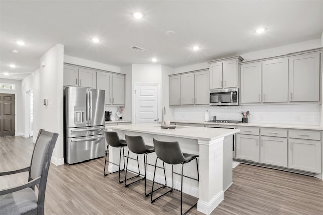 kitchen with a kitchen bar, gray cabinetry, light hardwood / wood-style flooring, stainless steel appliances, and a kitchen island with sink