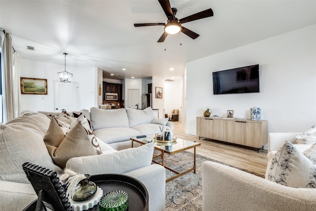 living room with ceiling fan with notable chandelier and light wood-type flooring