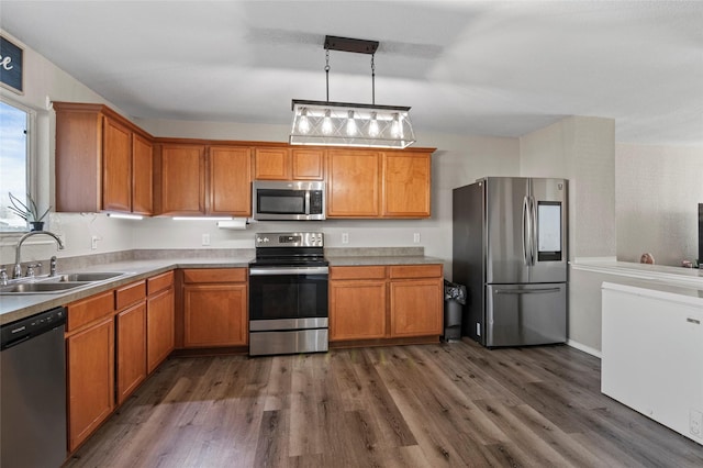 kitchen with appliances with stainless steel finishes, sink, dark wood-type flooring, and decorative light fixtures