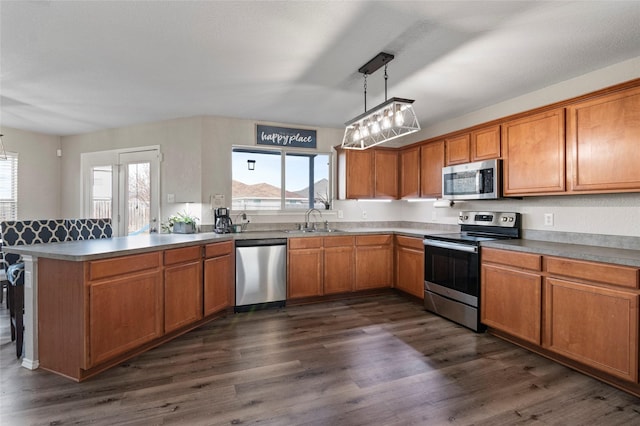 kitchen with pendant lighting, sink, dark hardwood / wood-style flooring, kitchen peninsula, and stainless steel appliances