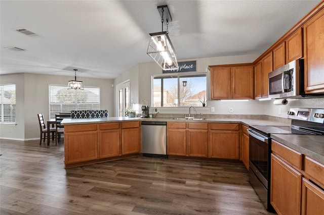 kitchen featuring pendant lighting, sink, kitchen peninsula, stainless steel appliances, and dark wood-type flooring