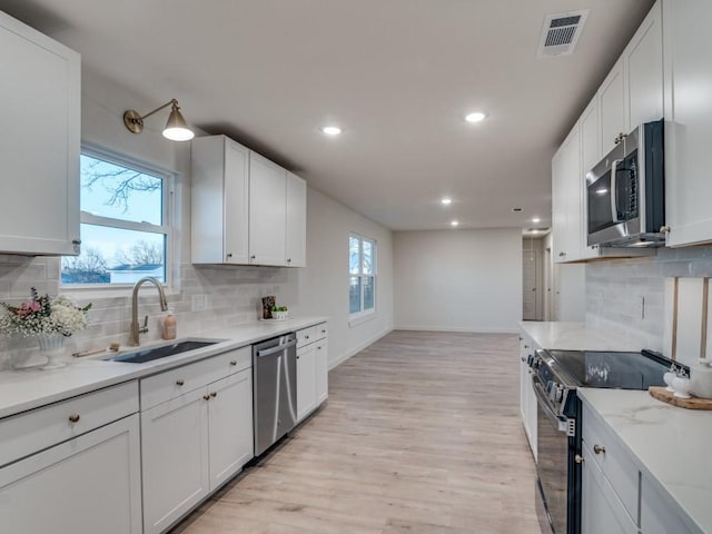 kitchen with light wood finished floors, visible vents, white cabinets, stainless steel appliances, and a sink