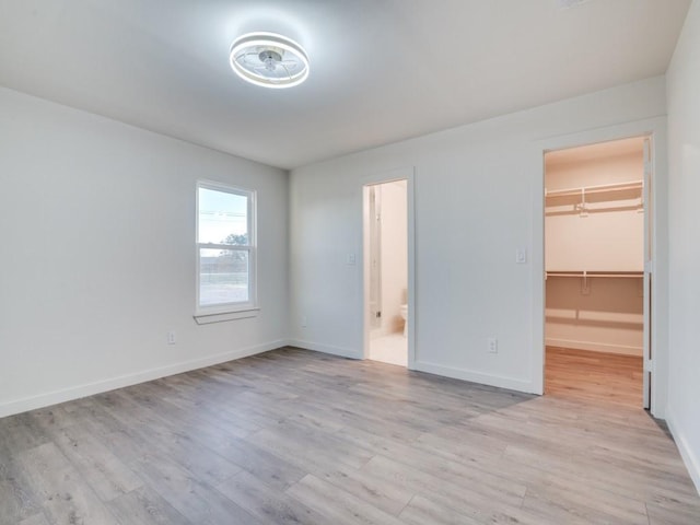 unfurnished bedroom featuring a spacious closet, light wood-type flooring, connected bathroom, and baseboards