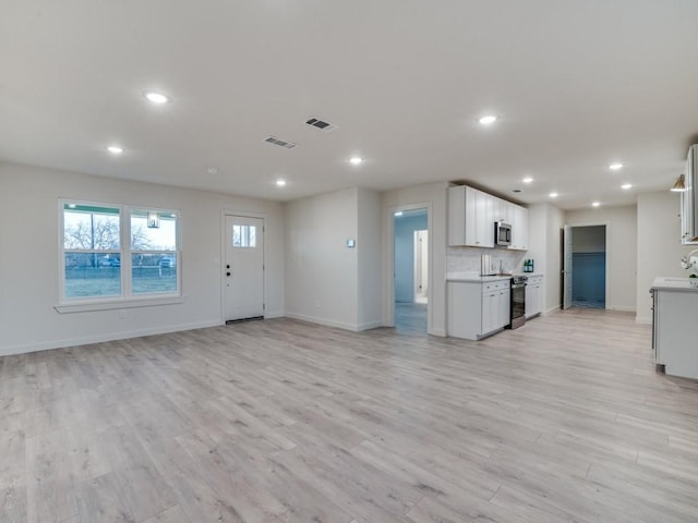 kitchen featuring electric stove, stainless steel microwave, visible vents, light wood-style floors, and open floor plan