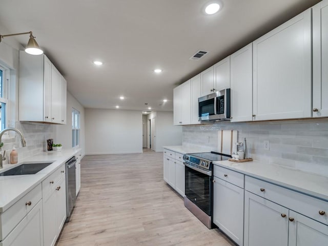 kitchen featuring a sink, visible vents, light countertops, appliances with stainless steel finishes, and light wood finished floors