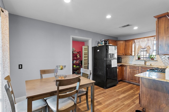 kitchen with sink, black fridge, light stone counters, light hardwood / wood-style floors, and decorative backsplash