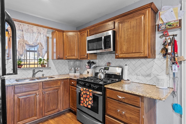 kitchen with sink, light stone counters, light hardwood / wood-style flooring, stainless steel appliances, and backsplash