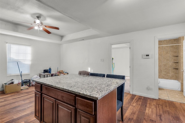 kitchen featuring a breakfast bar area, a tray ceiling, dark hardwood / wood-style flooring, a kitchen island, and ceiling fan